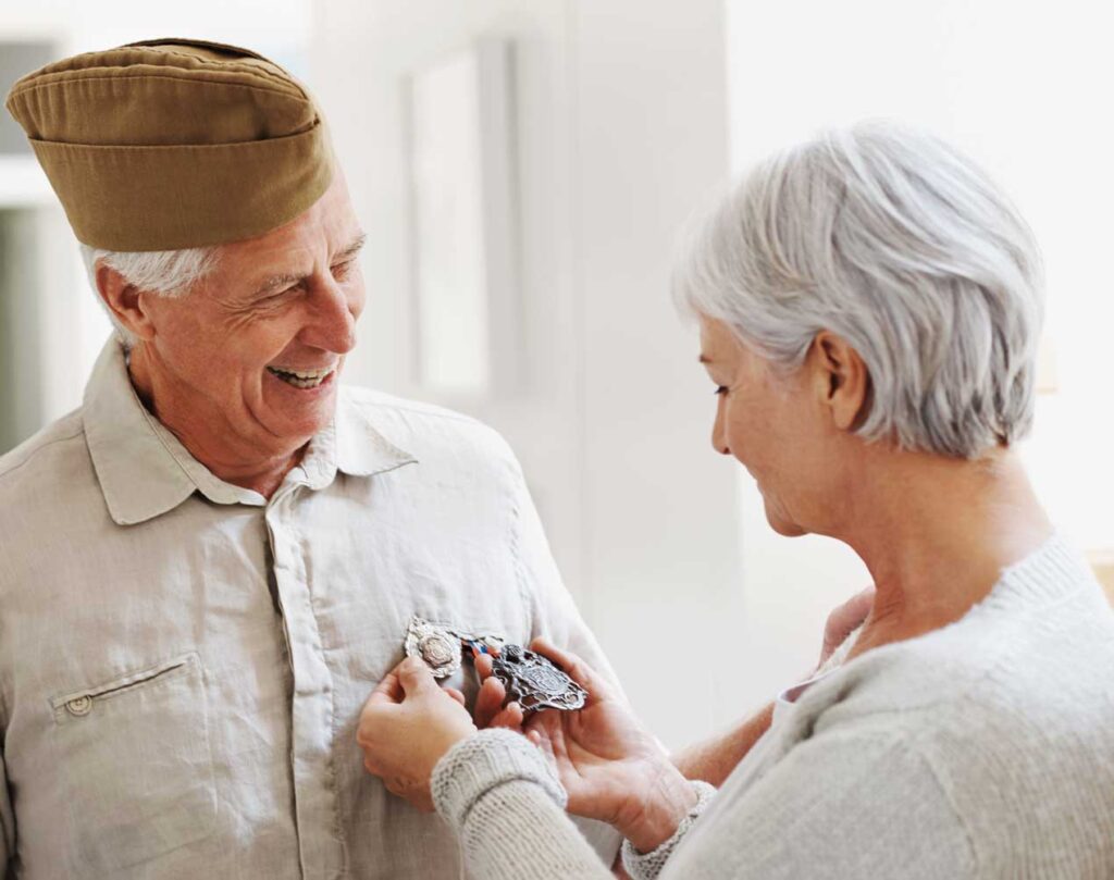 elderly veteran smiling at wife who is admiring his service medals
